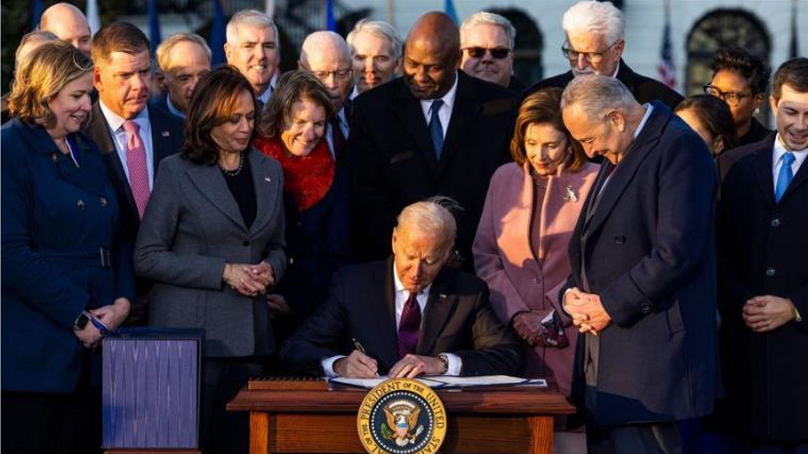 A group of political figures gathered around President Biden as he signs the Infrastructure Bill