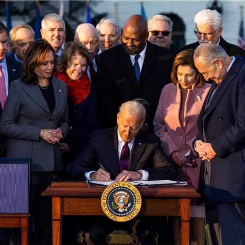 A group of political figures gathered around President Biden as he signs the Infrastructure Bill
