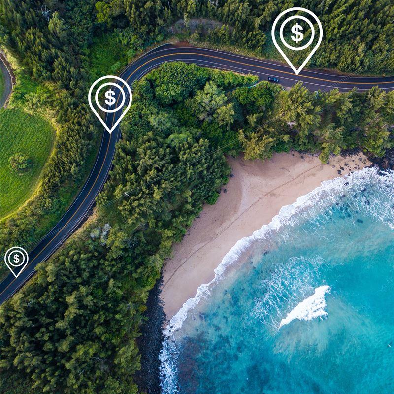 An aerial view of a highway in Hawaii, with illustrations of dollar signs conveying road usage charges.