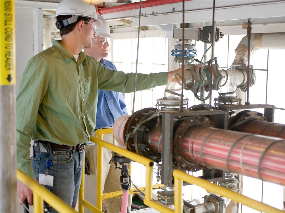 two men in construction hats inspecting a series of pipes