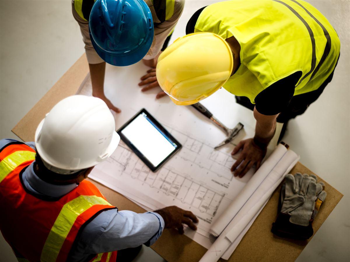 3 people in hard hats looks at plans